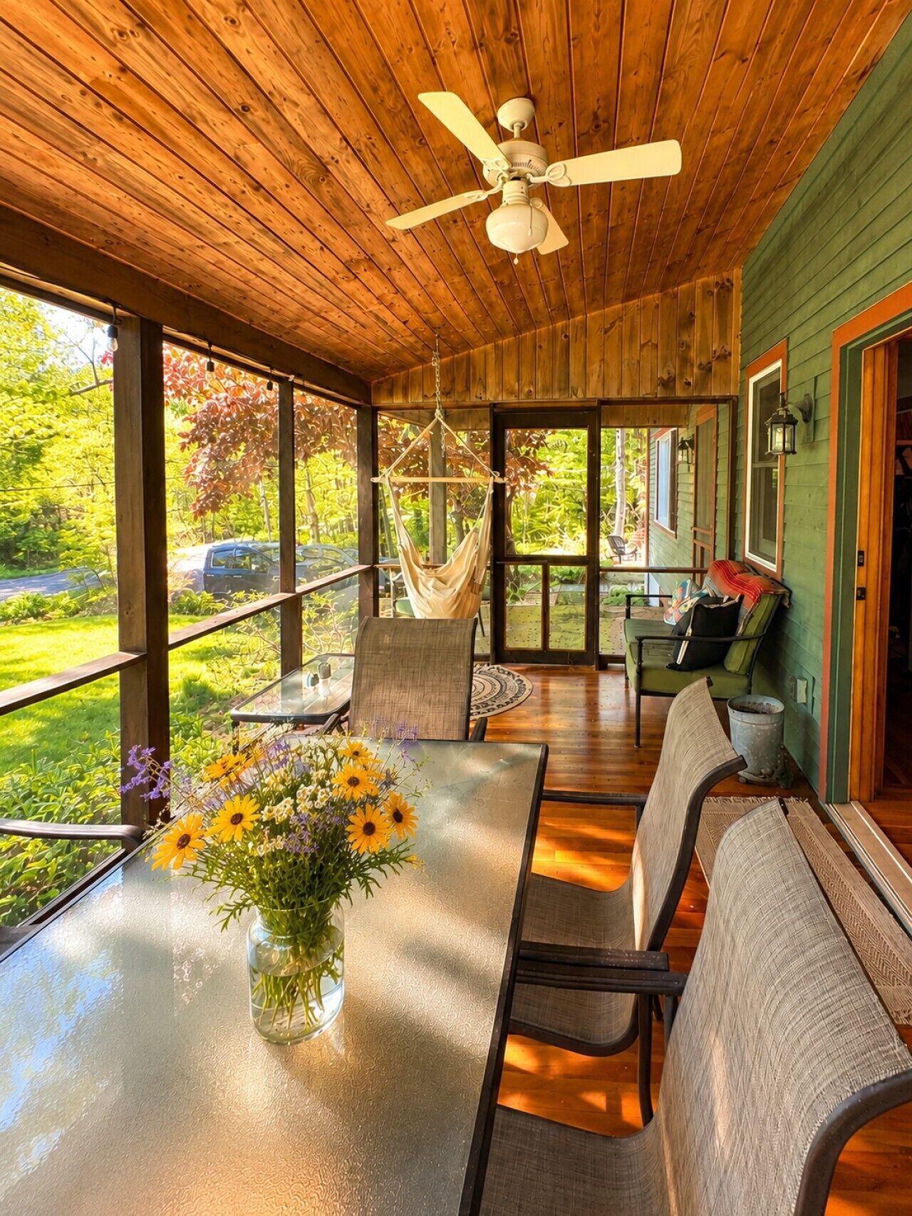 A wooden deck with a glass table, chairs, and a hanging chair.