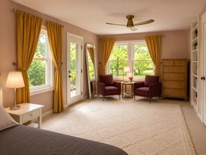 A bedroom with a bed, two armchairs, a small table, a dresser, and a ceiling fan. - The Woodland Retreat (Essex Junction)