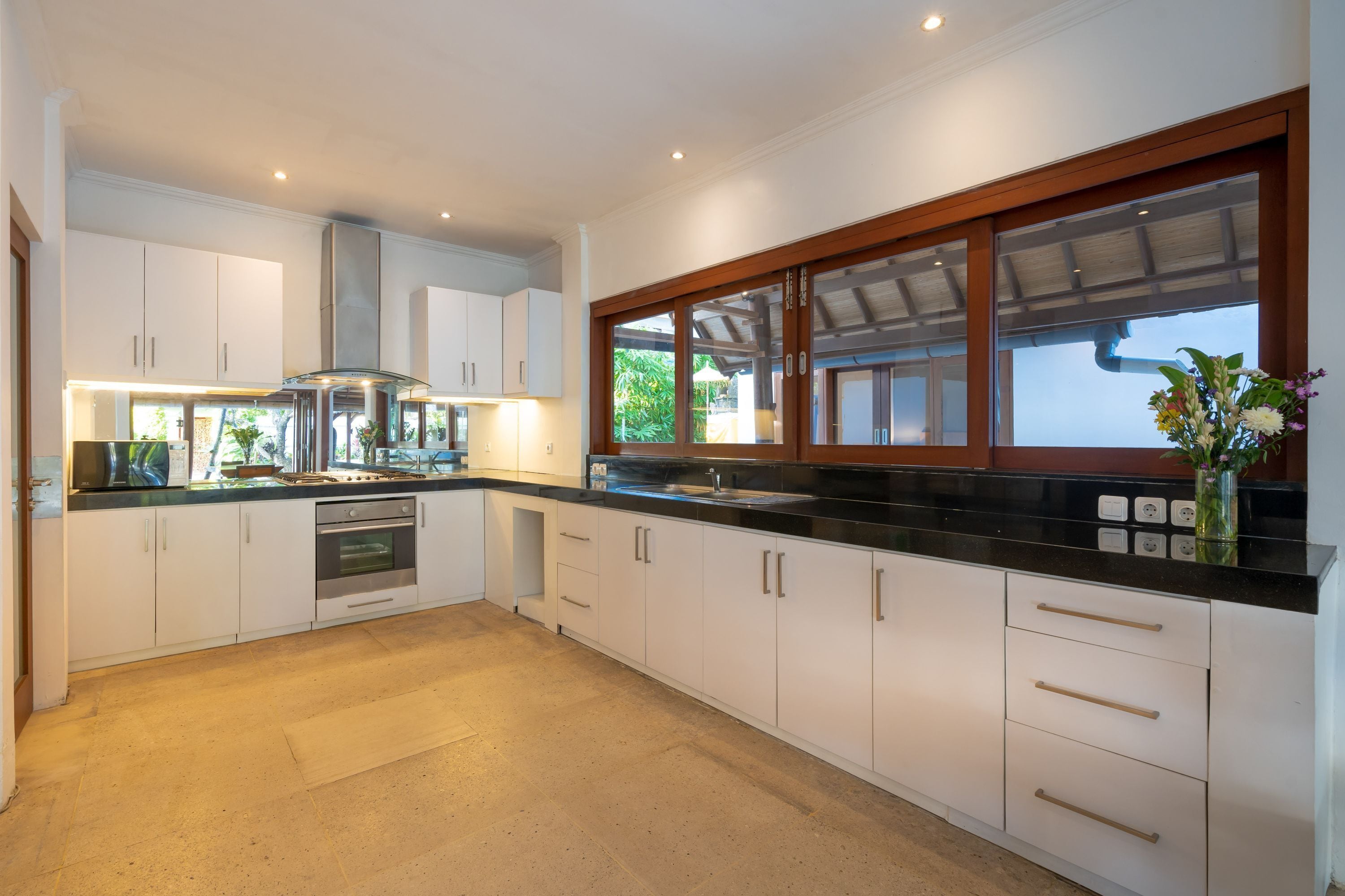A modern kitchen with white cabinetry, stainless steel appliances, and a large window with a view of greenery.