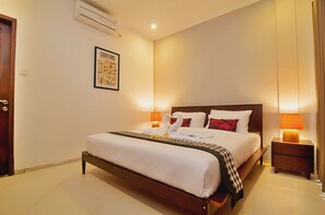 A hotel room with a bed, bedside lamps, a framed poster on the wall, and an air conditioning unit. - The Mawar Estate in Seminyak (Keroboken Kelod)