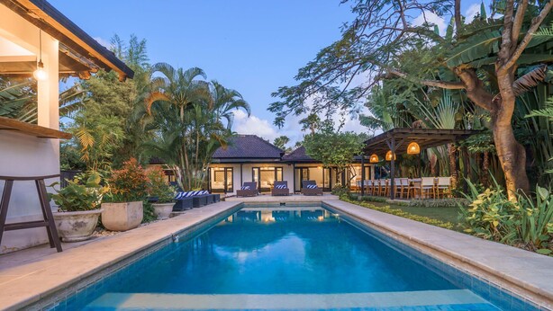 A swimming pool with lounge chairs and a covered seating area, surrounded by tropical vegetation. - The Aryana Estate in Seminyak (Keroboken Kelod)