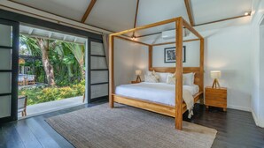A room with a four-poster bed, a wooden nightstand, a bedside lamp, and a view of a tropical garden. - The Aryana Estate in Seminyak (Keroboken Kelod)