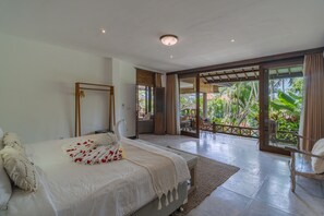 A bedroom with a bed, a wooden chair, and a view of a tropical garden through a glass door. - Jessica Estate in Canggu (Tibubeneng)