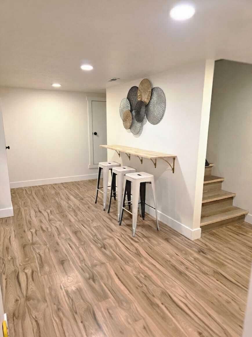 Une pièce avec un plancher en bois, un mur blanc orné d’une assiette décorative et un escalier.