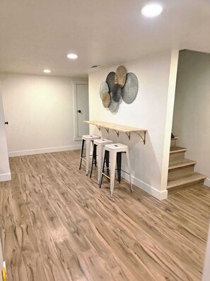 A room with a wooden floor, a white wall with a decorative plate, and a staircase. - Private 2BR Basement Suite / Patio•Cinema•Fire Pit (Sandy)
