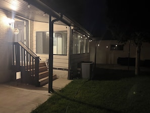 A residential building with a wooden staircase, a covered porch, and a visible trash bin. - Private 2BR Basement Suite / Patio•Cinema•Fire Pit (Sandy)