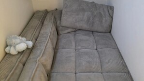 Un espacio de descanso pequeño y cerrado con un colchón y almohada acolchados de color gris. Un peluche está situado a la izquierda.