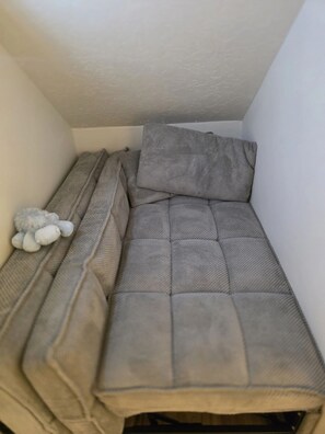 A small, enclosed sleeping area with a grey quilted mattress and a grey pillow. A plush toy is placed on the left side. - Private 2BR Basement Suite / Patio•Cinema•Fire Pit (Sandy)