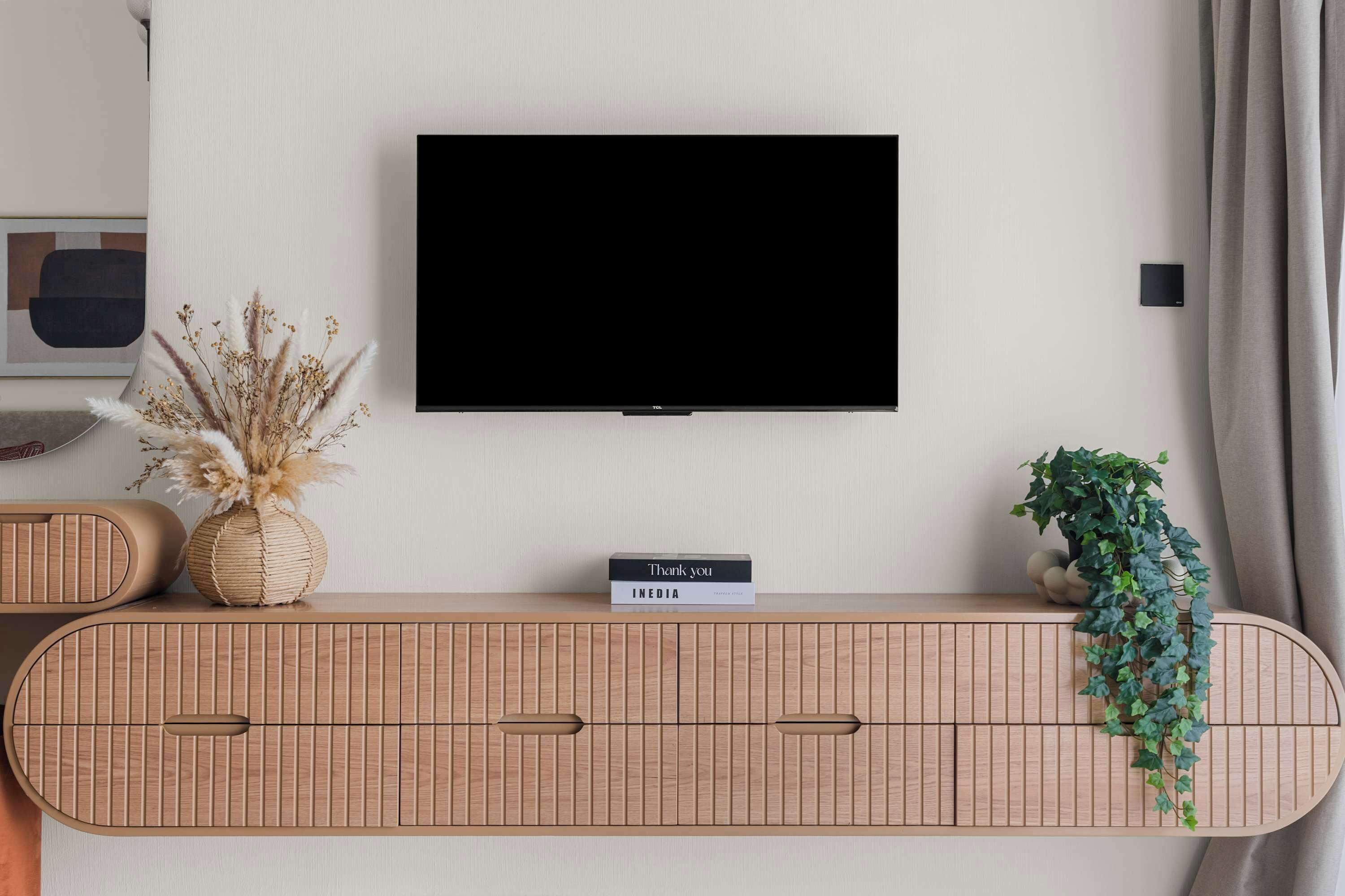 A modern living room with a mounted television, a wooden console table with decorative items, and a potted plant.