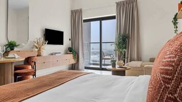 A hotel room with a bed, a desk, a television, and a balcony with curtains.