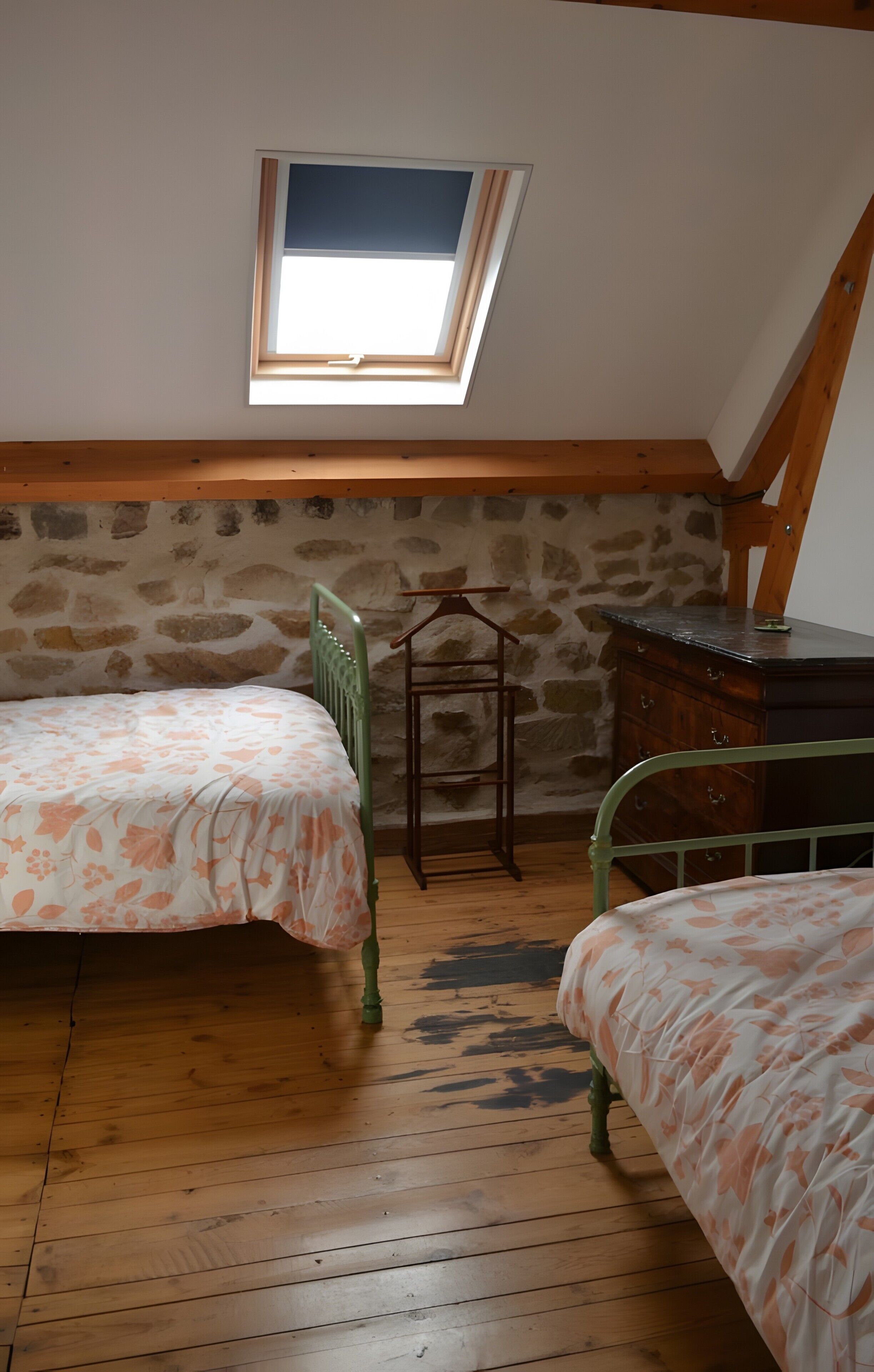 Een kleine zolderkamer met twee bedden, een houten dressoir en een stenen muur.