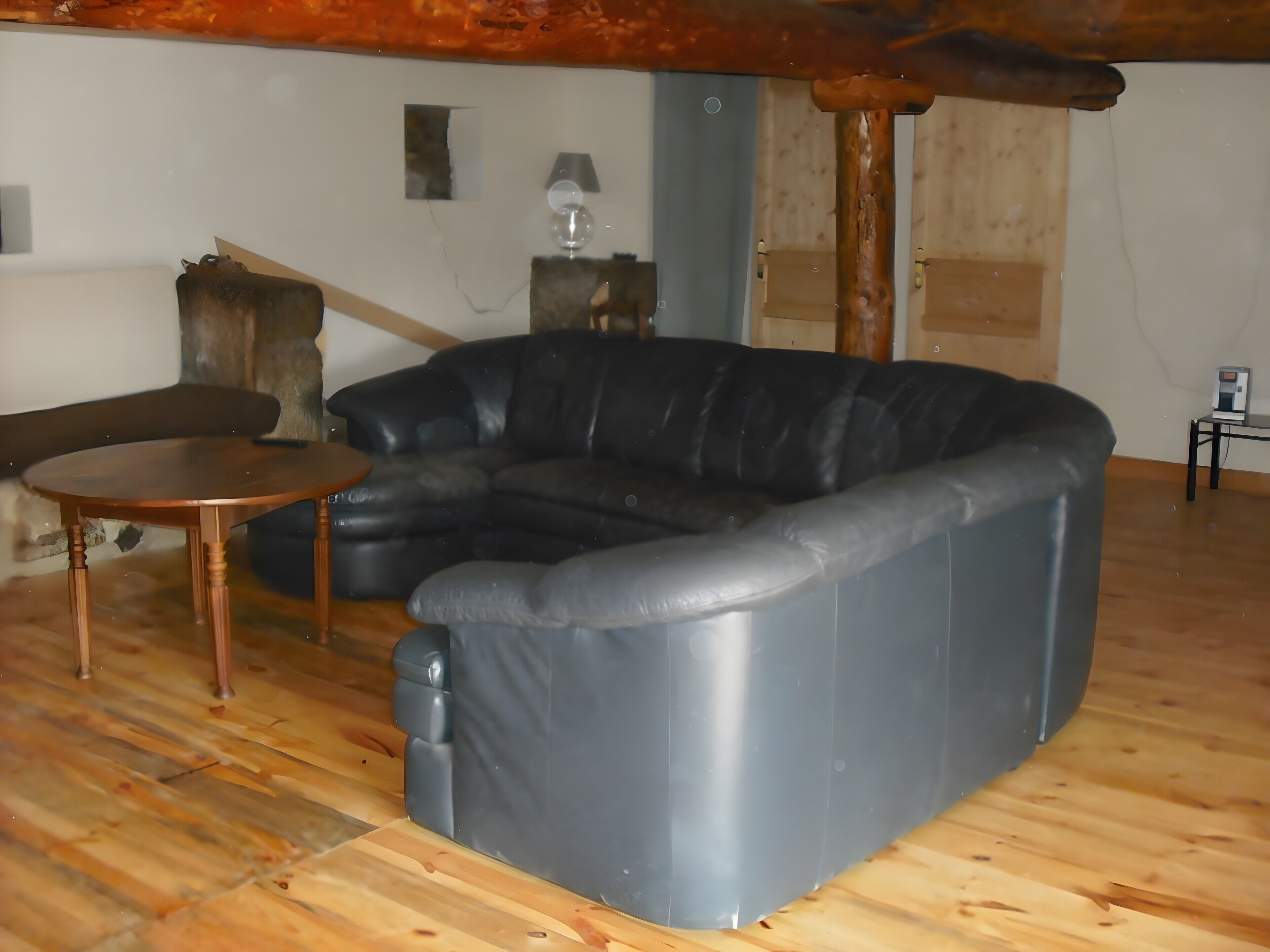 Une pièce avec un canapé en cuir noir, une petite table ronde en bois et une lampe fixée au mur.