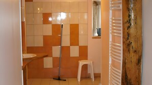 A bathroom with a tiled floor, a mop, a white stool, and a wooden beam.