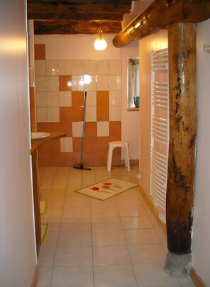 A bathroom with a tiled floor, a mop, a white stool, and a wooden beam.