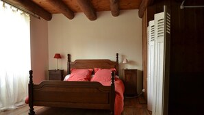 A wooden bed with a headboard, a nightstand with a lamp, and a wardrobe in a room with wooden flooring and a sloped ceiling.