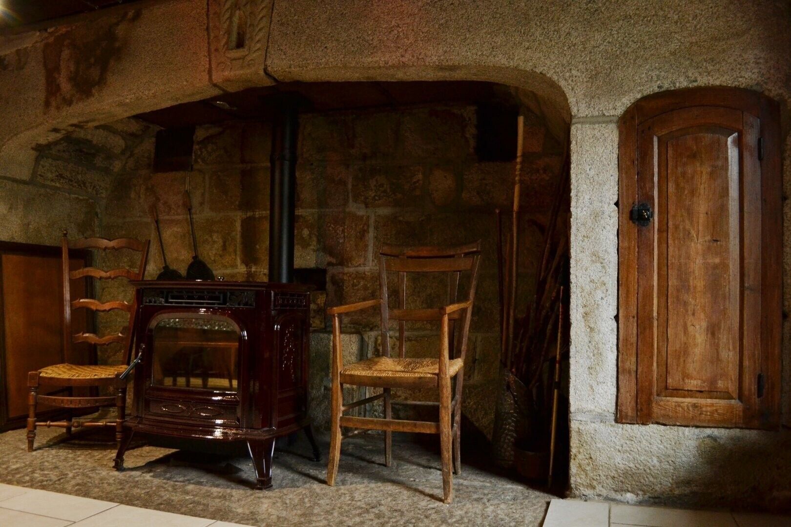 Ein Zimmer mit Steinwand, Holztür und einem Vintage-Radio. Zwei Holzstühle und ein Kamin sind ebenfalls vorhanden.