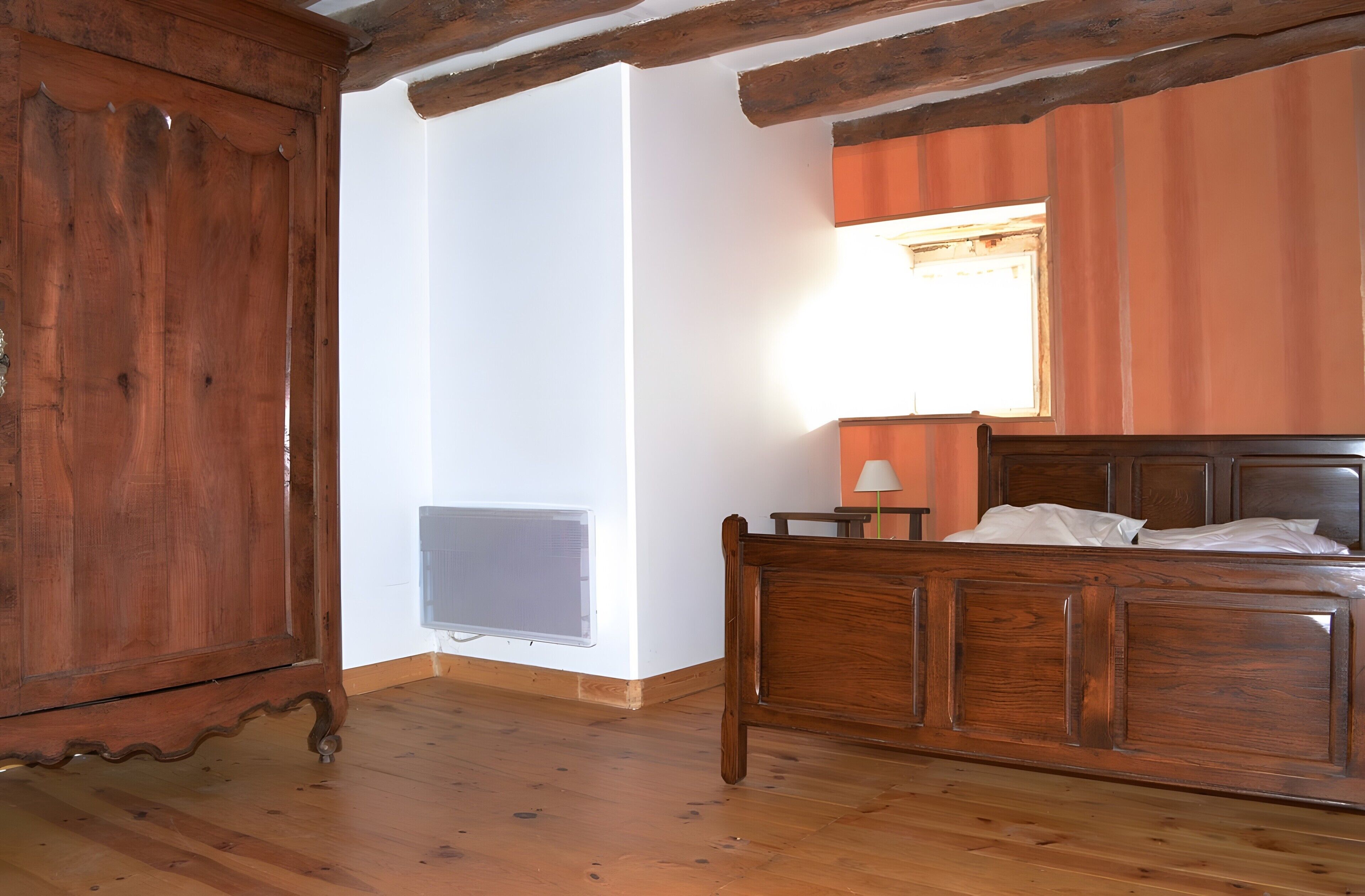 Une pièce avec un lit en bois, un radiateur et une fenêtre avec une lampe.