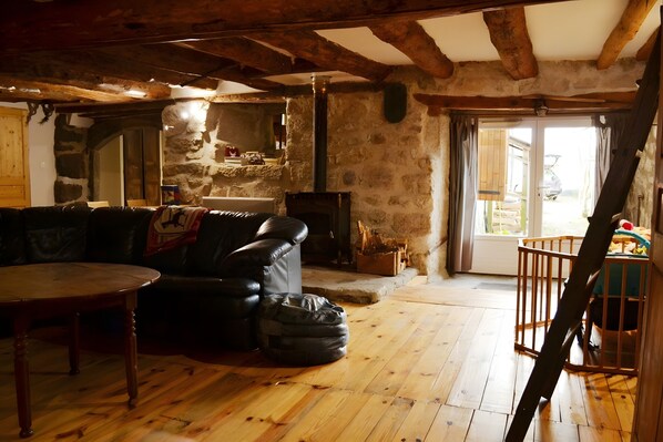 A rustic interior with exposed wooden beams, a stone wall, a fireplace, a leather sofa, and a wooden table.