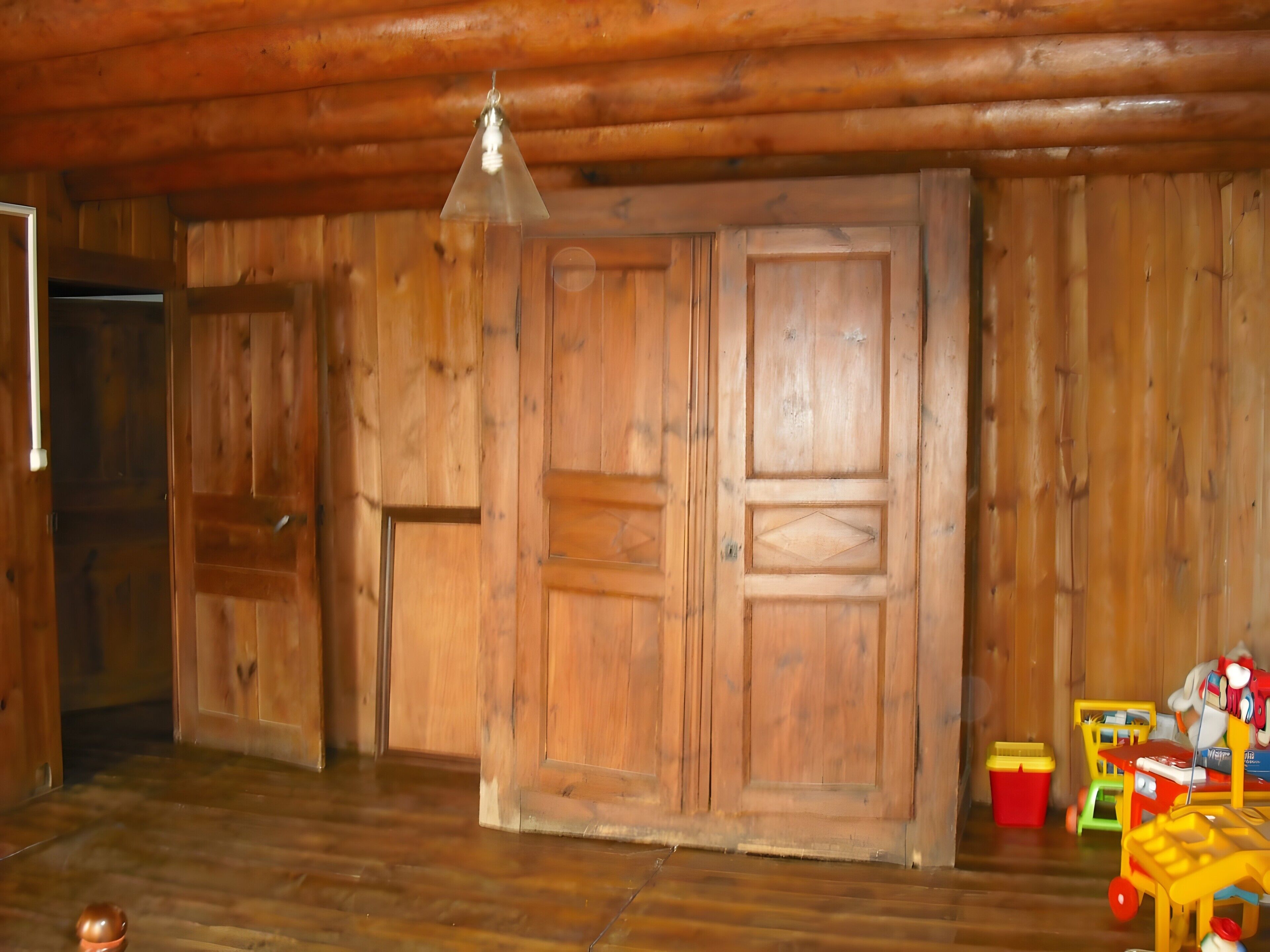 Un intérieur en bois avec une grande porte en bois, un luminaire suspendu et un ensemble de jouets représentant un train.