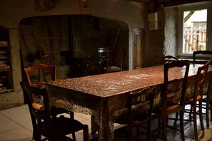 A rustic dining area with a stone archway, wooden chairs, and a tiled floor.