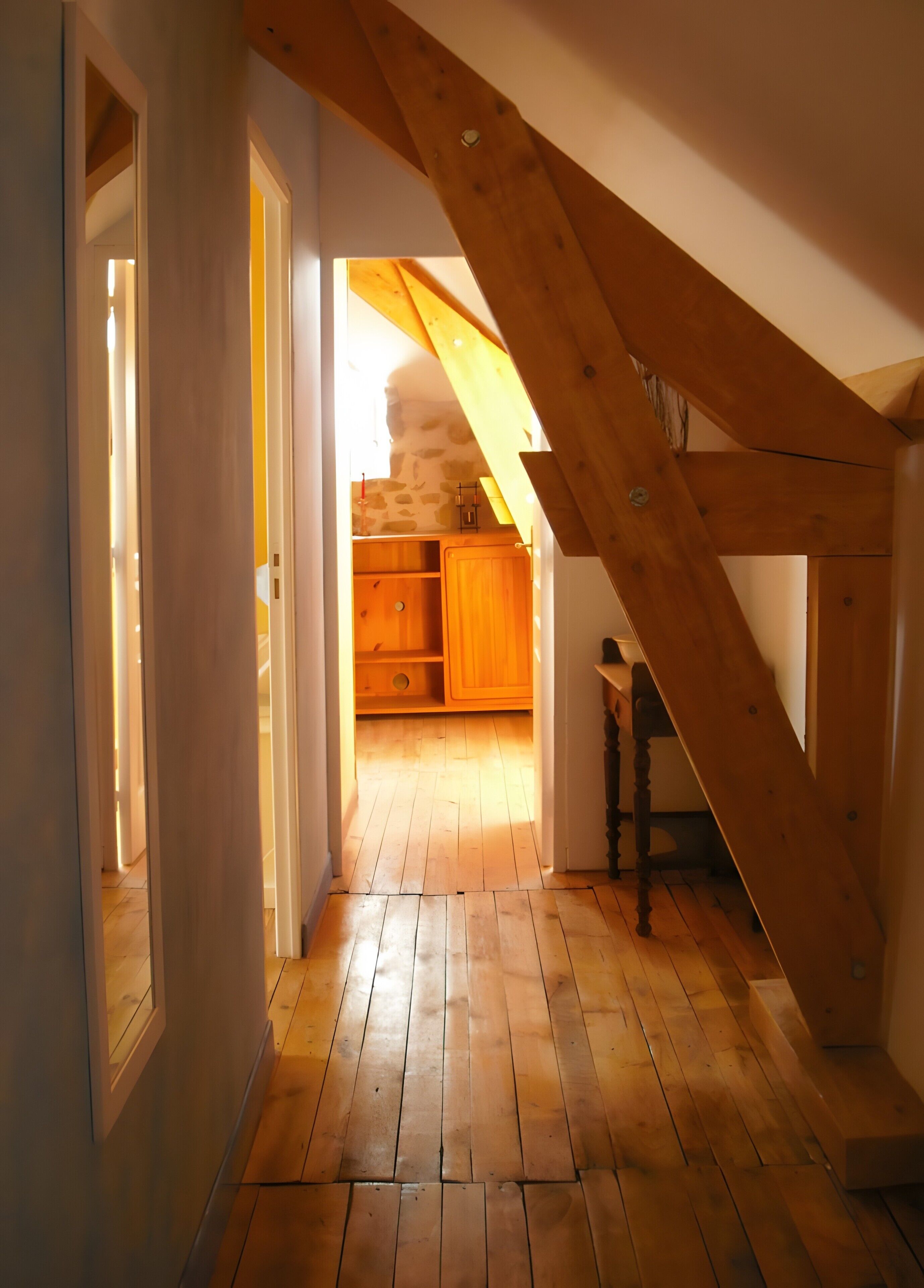 Un escalier en bois mène à une cuisine surélevée, dotée d’un mur en pierre et de meubles de rangement en bois.
