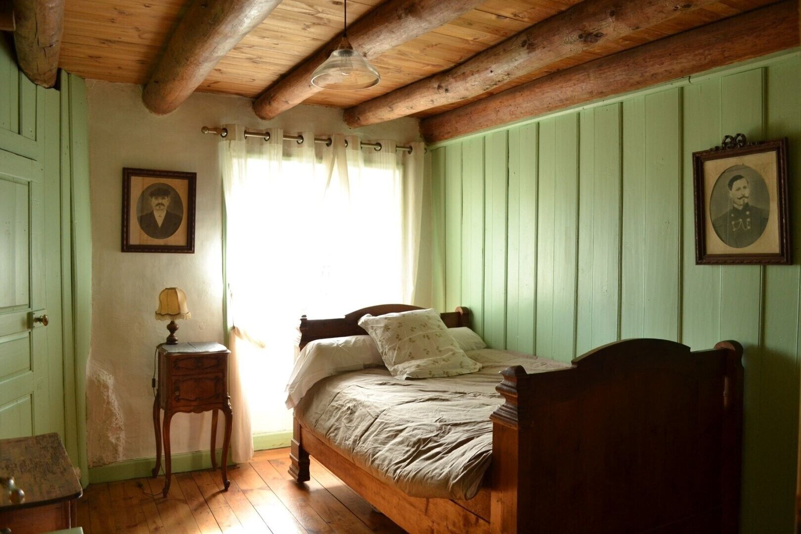 A room with a wooden bed, a nightstand with a lamp, and two framed pictures on the wall.