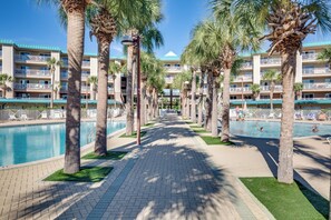 Ein Hotelpoolbereich mit Palmen, blauem Himmel und Blick auf das Hotelgebäude im Hintergrund.