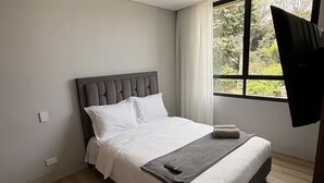 Quarto de hotel moderno com uma cama grande, janela com cortinas e uma TV de tela plana na parede.