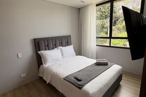 A modern hotel room with a large bed, a window with curtains, and a flat-screen TV mounted on the wall. - Balcony, birds, and nature · 2 bedrooms · Bogotá (Bogotá)