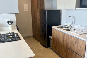 Une cuisine avec un réfrigérateur noir, des armoires en bois, un plan de travail blanc et un évier en acier inoxydable.