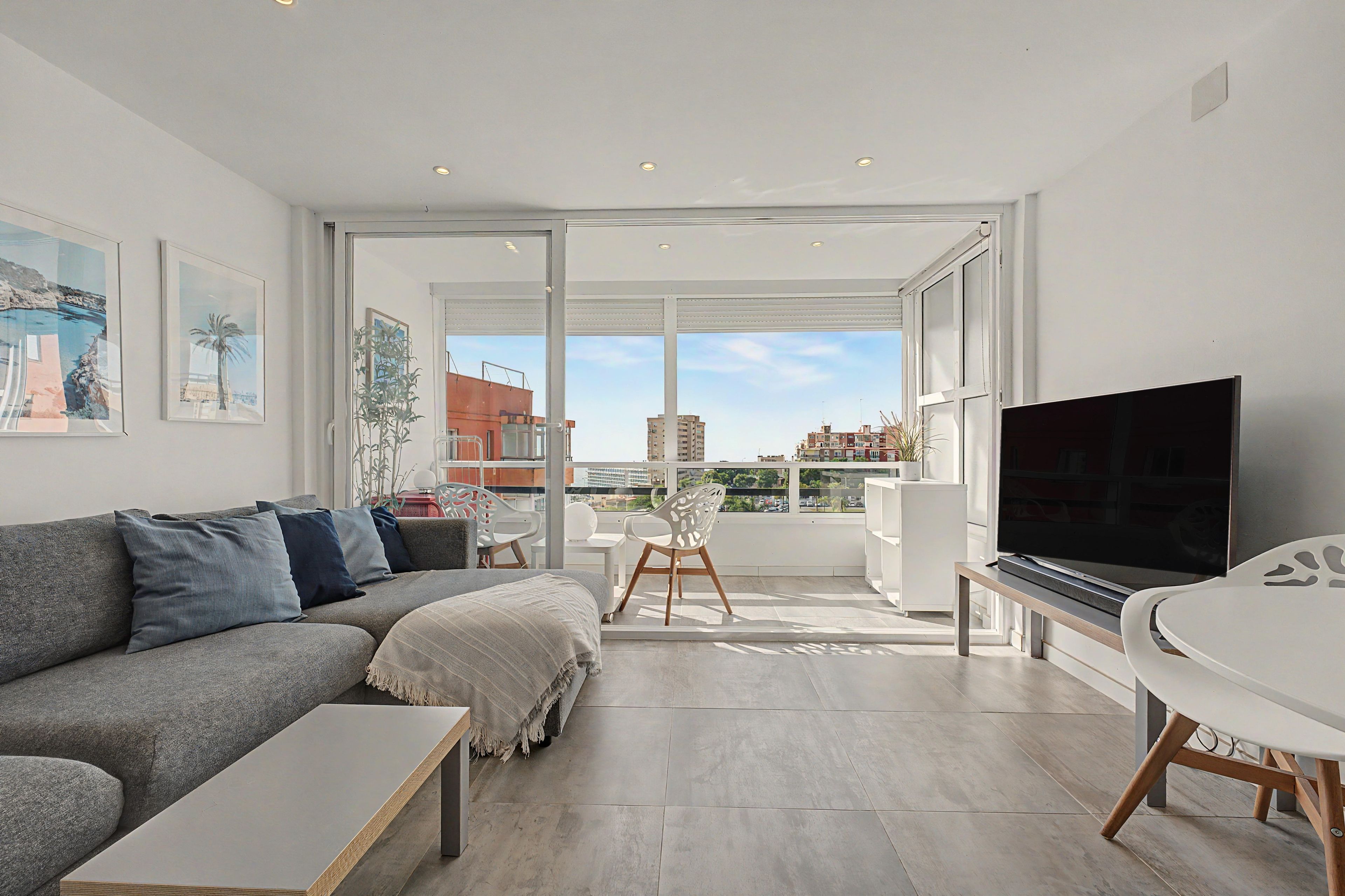 A modern living room with a grey sofa, a flat-screen TV, and a dining area with a white table and chairs.