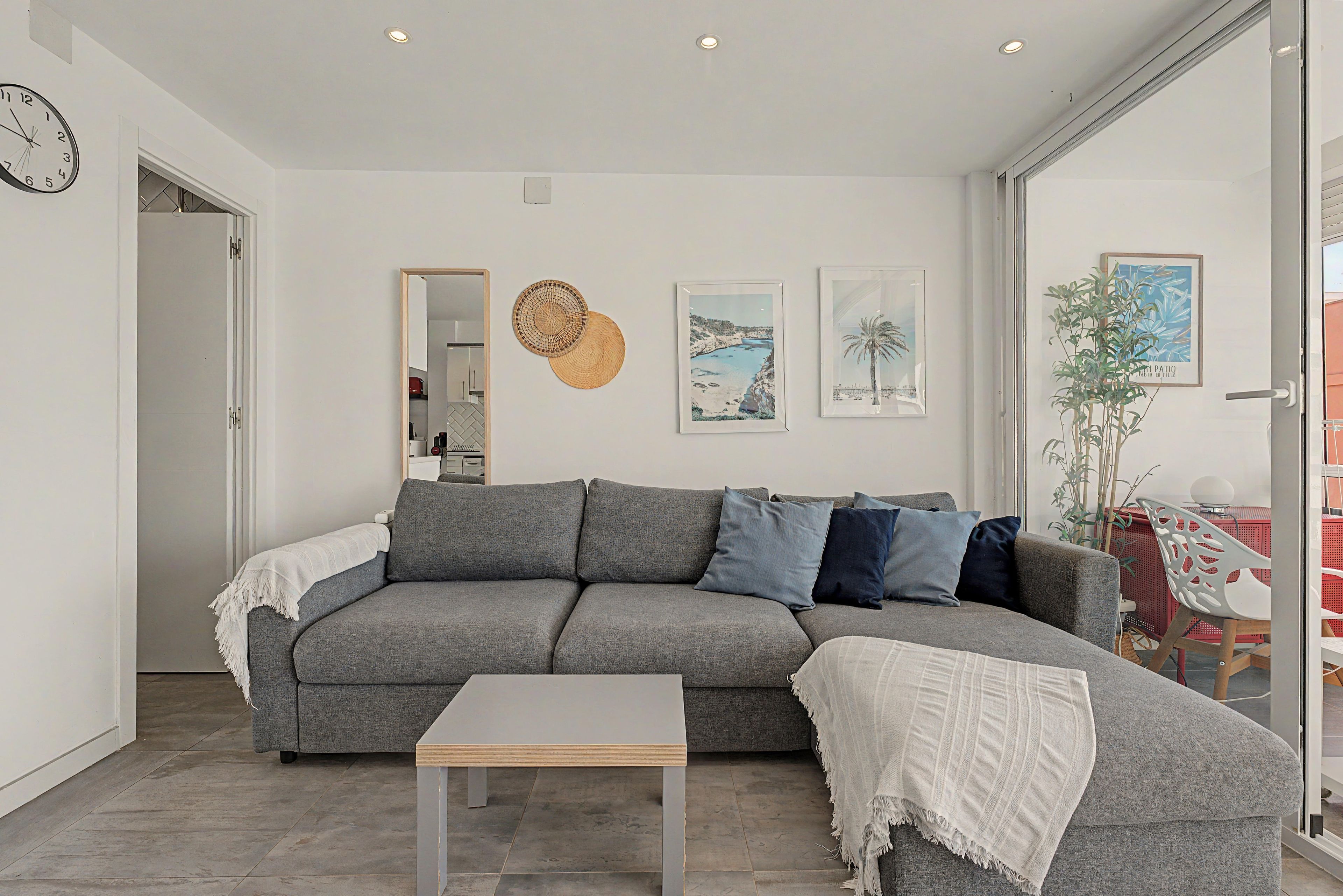 Un salon moderne avec un canapé d’angle gris, une petite table blanche et une grande fenêtre.