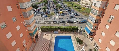A residential area with a swimming pool, parking lot, and apartment buildings.