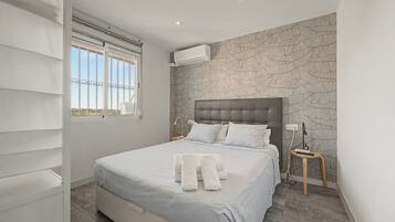 Une chambre à coucher avec un lit, une fenêtre, un climatiseur fixé au mur et un papier peint à motifs.