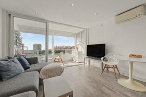 A modern living room with a sofa, a TV, a dining table, and chairs. - Costa del Sol Apartment with Balcony, Wi-Fi, Air Conditioning (Torremolinos)