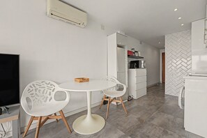 Une cuisine moderne avec des meubles blancs, une table de salle à manger ronde accompagnée de deux chaises, et un climatiseur intégré au-dessus du comptoir.