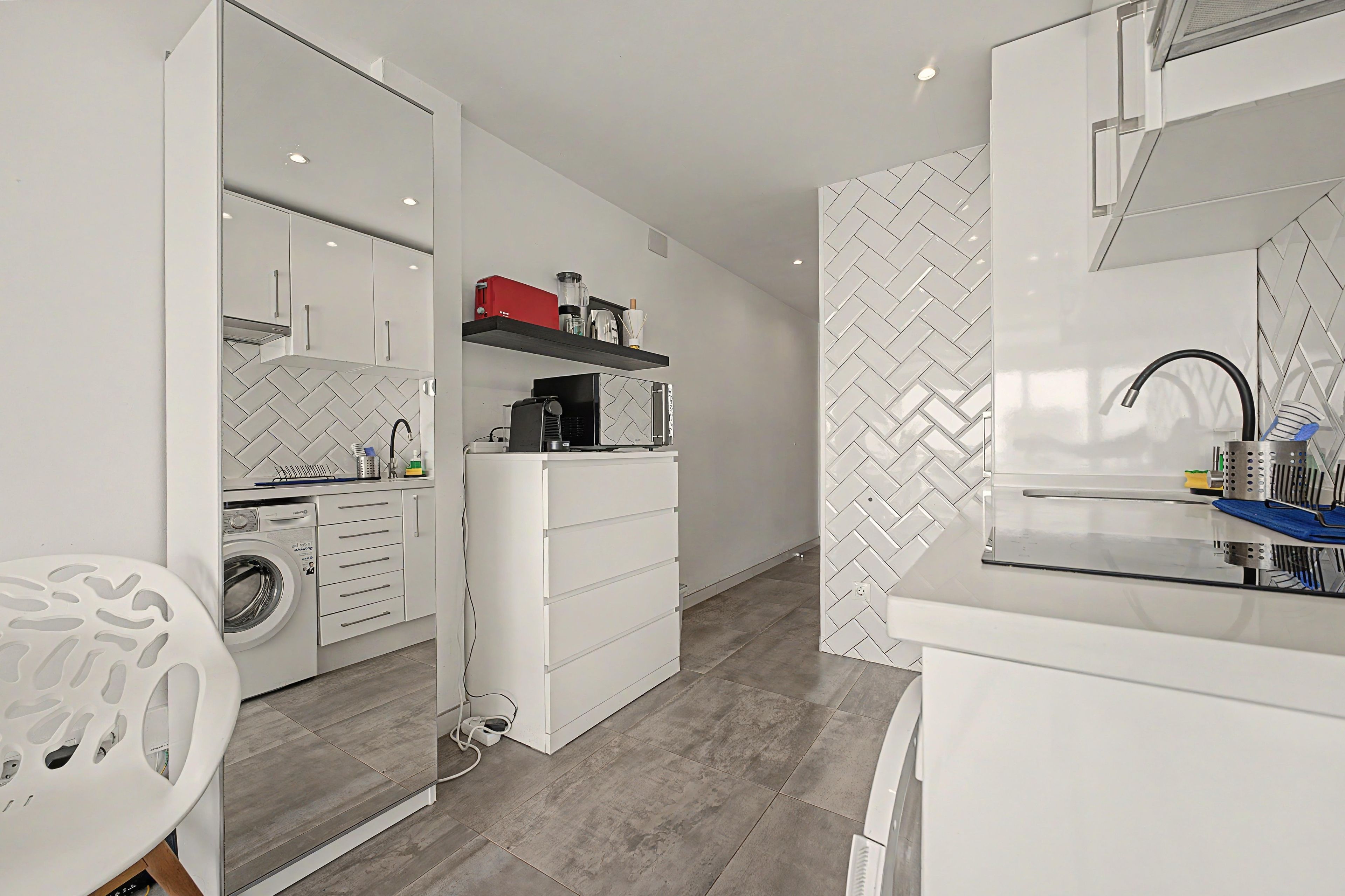 Une cuisine moderne avec des meubles blancs, un lave-linge encastré et un plan de travail doté d’un évier.