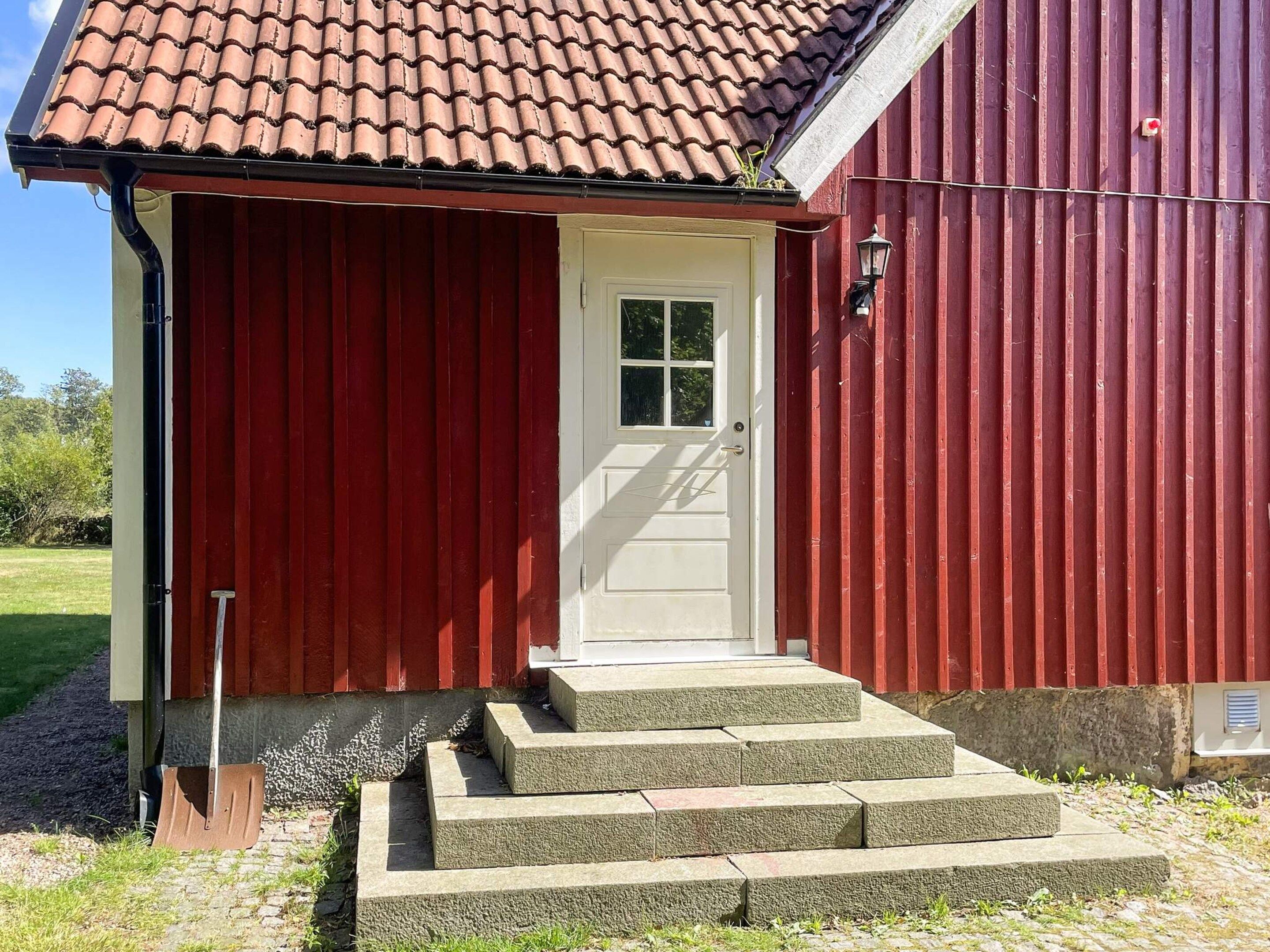 A red building with a white door and a small porch with steps leading up to it.