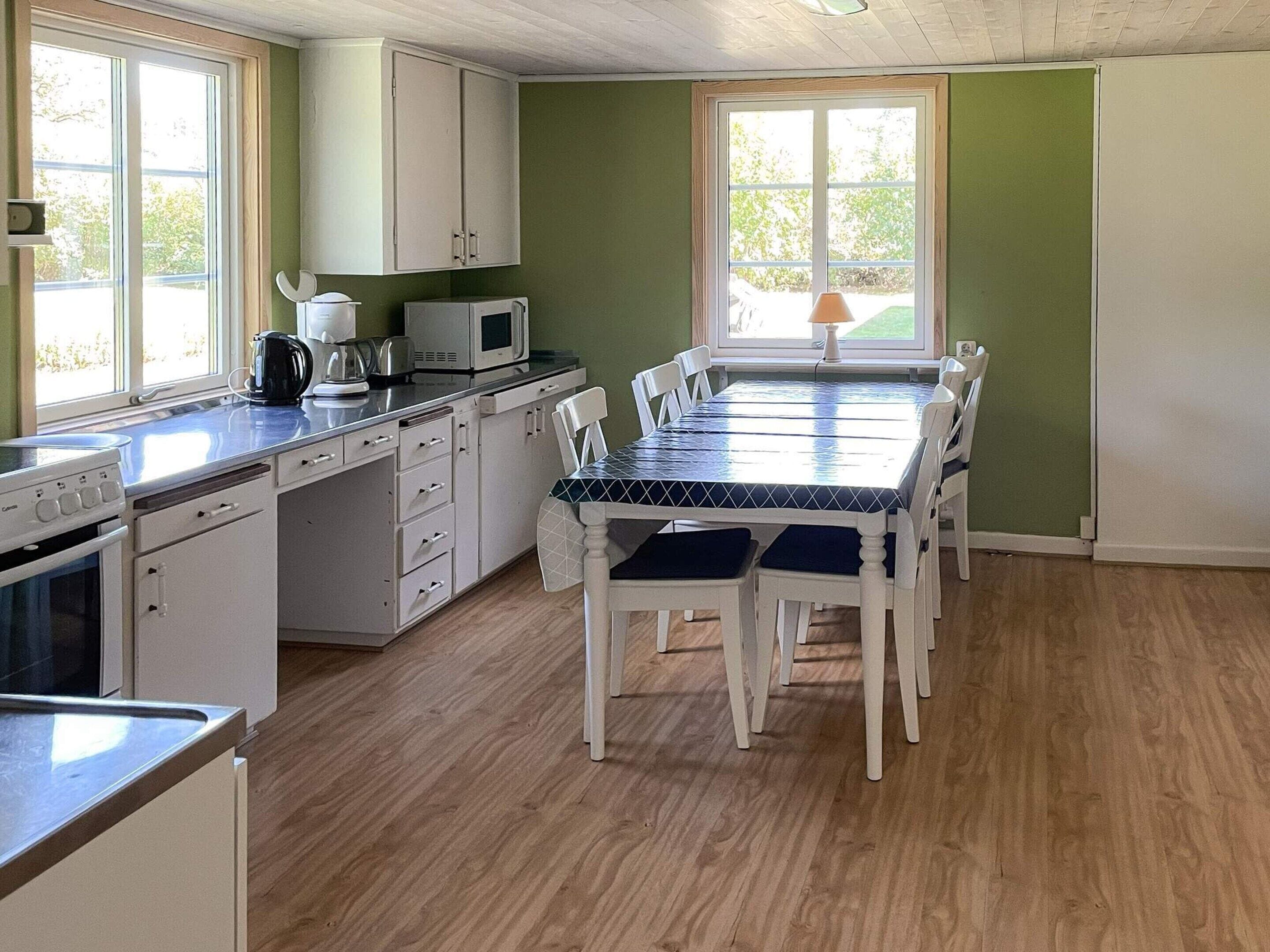 A kitchen with white cabinets, a microwave, and a stove. There is a dining table with chairs and a window with a view of greenery.