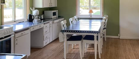 A kitchen with white cabinets, a microwave, and a stove. There is a dining table with chairs and a window with a view of greenery.