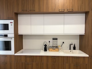 Una cocina con armarios de madera, microondas, horno, cafetera y un lavamanos.