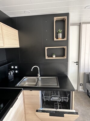 A modern kitchen with a black countertop, stainless steel sink, wooden cabinets, and built-in dishwasher.
