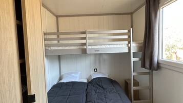 Een slaapkamer met stapelbed, een raam, een houten garderobe en een plafondlamp.