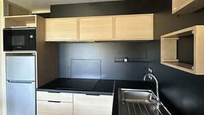 A compact kitchen with a black countertop, stainless steel sink, and wooden cabinets. - The Scandola Reserve (Appietto)