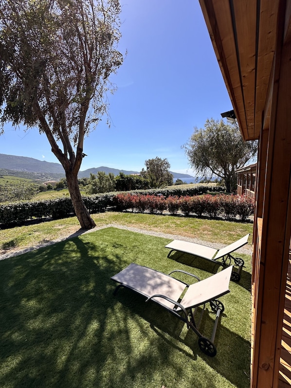A patio with two sun loungers, a tree, and a view of a distant landscape.
