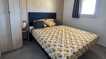 Een slaapkamer met een bed, nachtkastje, lamp, raam met gordijnen en een plafondlamp.