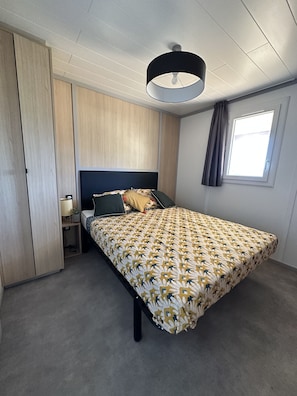 A bedroom with a bed, a nightstand, a lamp, a window with curtains, and a ceiling light fixture.