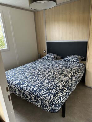 Ein Einzelbett mit einem gemusterten Bettbezug in einem Zimmer, das ein Holz-Kopfstück und ein Fenster hat.