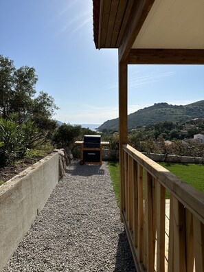 Un balcone con barbecue, pavimento in ghiaia e vista su un pendio collinare e edifici in lontananza.