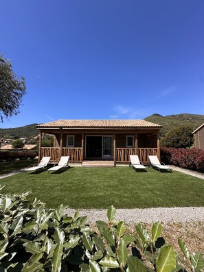 A house with a tiled roof, a front porch with two chairs, and a well-maintained lawn.